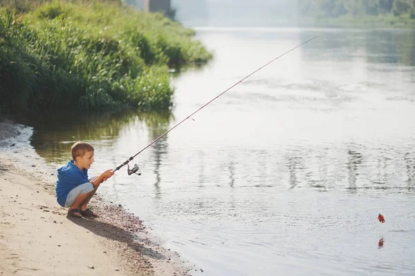 Счастливый мальчик с удочкой на берегу реки — стоковое фото