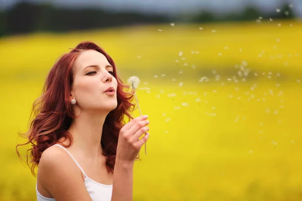 Beautiful woman blowing dandelion in the field — Stock Photo, Image