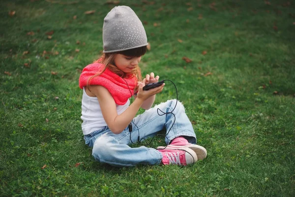 Çimlerin üstünde hareket eden telefon ile küçük kız — Stok fotoğraf