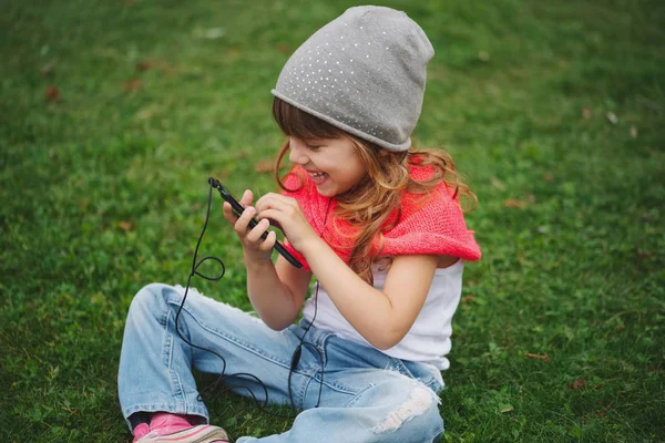 Malá holčička s mobilním telefonem na trávě — Stock fotografie