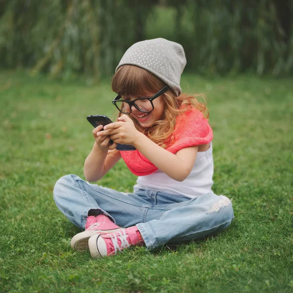 Çimlerin üstünde hareket eden telefon ile küçük kız — Stok fotoğraf