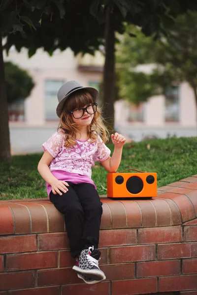 Little hipster girl listens music on wireless retro looking spea — Stock Photo, Image