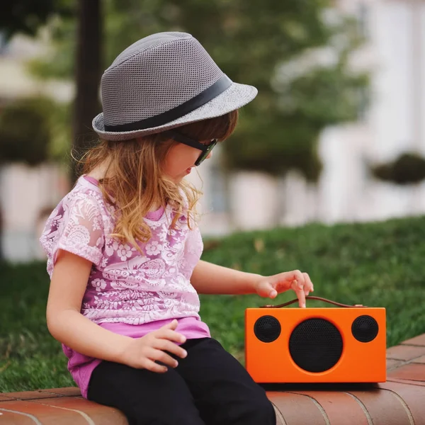 Little hipster girl listens music on wireless retro looking spea — Stock Photo, Image