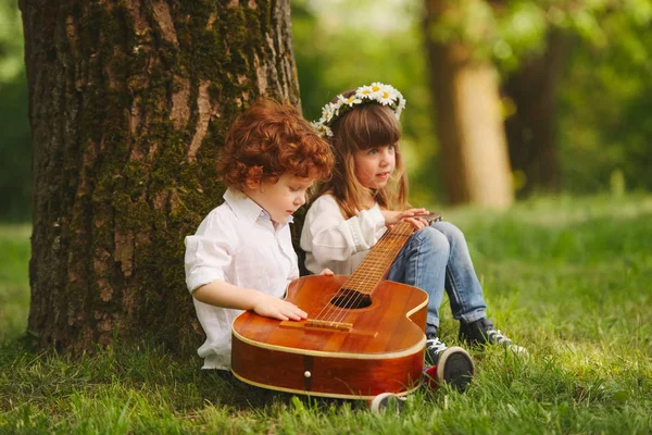 Niño y niña tocando la guitarra en el parque de verano — Foto de Stock