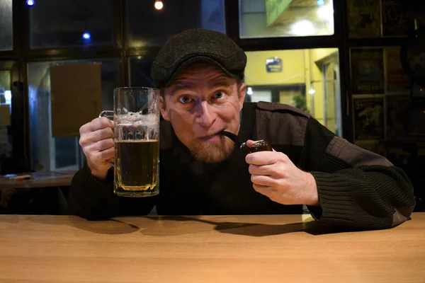 红头发的爱尔兰小伙子坐在酒吧里 喝着啤酒 脸上带着滑稽的表情抽着木管 — 图库照片