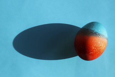 Paskalya için canlı renkli yumurtalar uzun gölgeli kırmızı ve mavi kağıtların üzerinde duruyor.