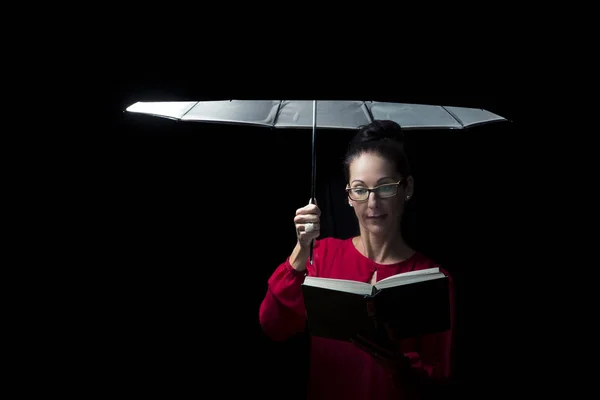 Beautiful woman with red dress reading a book in rain under an u