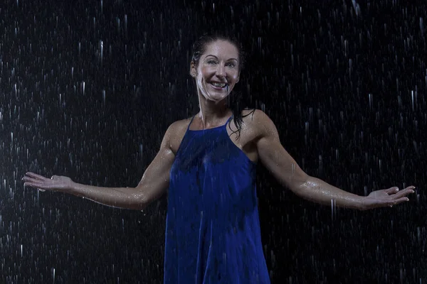 Beautiful woman in blue dress stands in rain at night