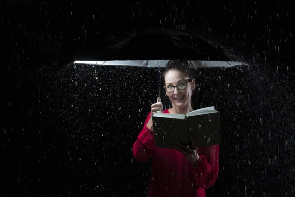Mulher bonita com vestido vermelho lendo um livro na chuva sob um u — Fotografia de Stock