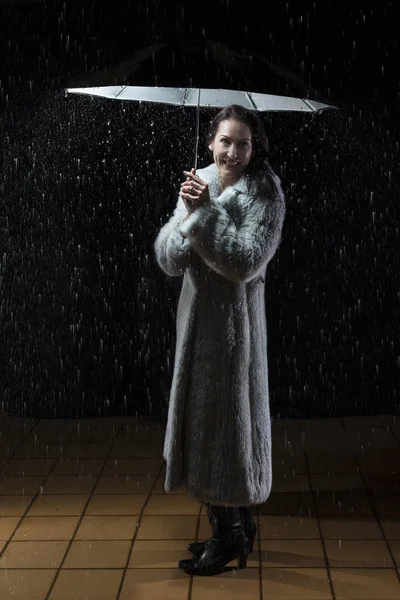 Beautiful woman with fur coat standing in rain under an umbrella — Stock Photo, Image