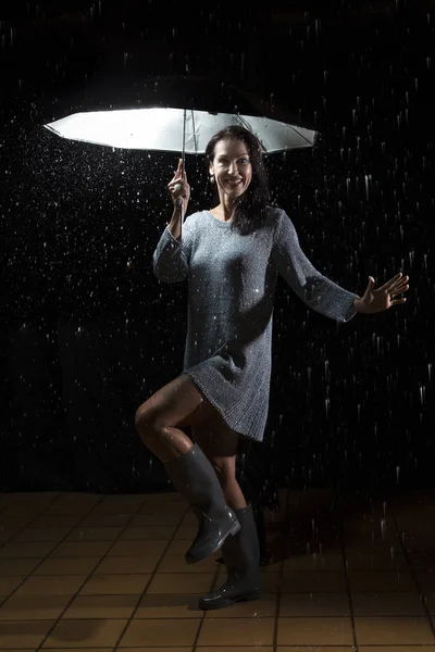 Schöne Frau mit silbernem Kleid, die im Regen unter einem Regenschirm tanzt — Stockfoto