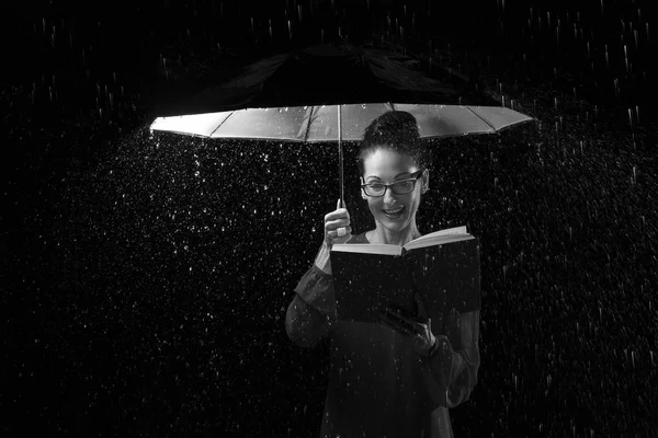 Hermosa mujer con vestido leyendo un libro bajo la lluvia bajo un umbre — Foto de Stock