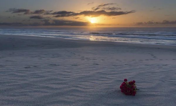 Ramo de flores rojas en la playa al amanecer con cielo nublado —  Fotos de Stock