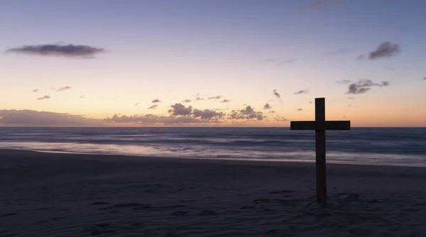 An old cross on sand dune next to the ocean with a calm sunrise — Stock Photo, Image