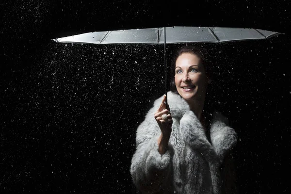 Hermosa mujer con abrigo de piel de pie bajo la lluvia bajo un paraguas — Foto de Stock