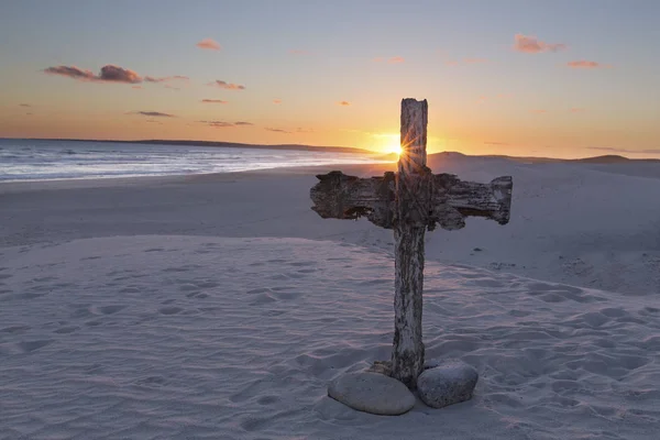 An old cross on sand dune next to the ocean with a calm sunrise — Stock Photo, Image