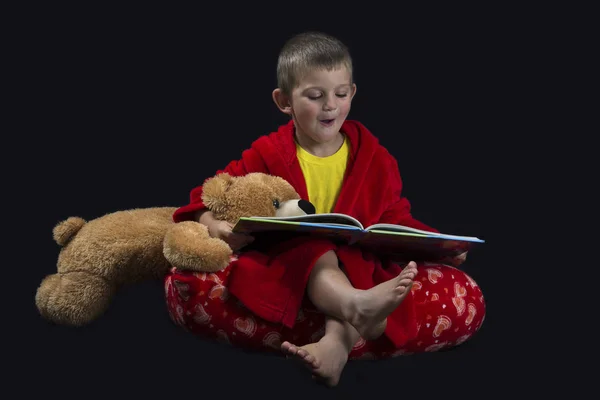 Funny boy with teddy bear reading a book before bed time — Stock Photo, Image