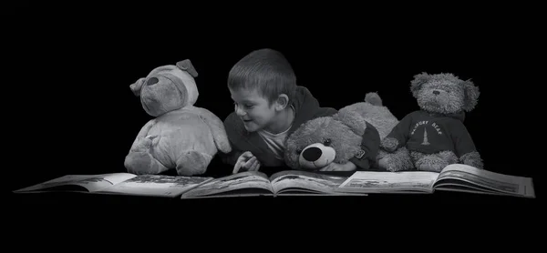 Funny boy with stuffed animals reading a book before bed time ar — Stock Photo, Image