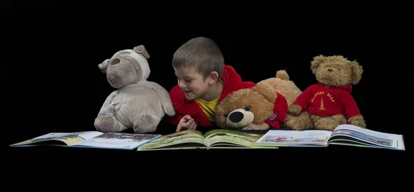 Funny boy with stuffed animals reading a book before bed time — Stock Photo, Image