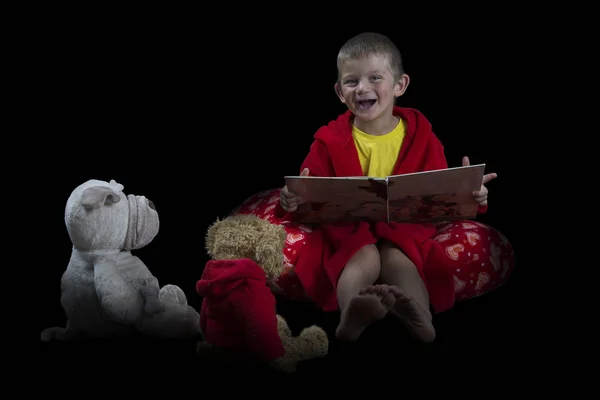 Смішний хлопчик з фаршированими тваринами читає книгу перед сном — стокове фото