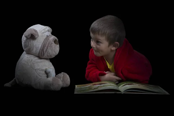 Funny boy with a stuffed dog reading a book for bed time — Stock Photo, Image