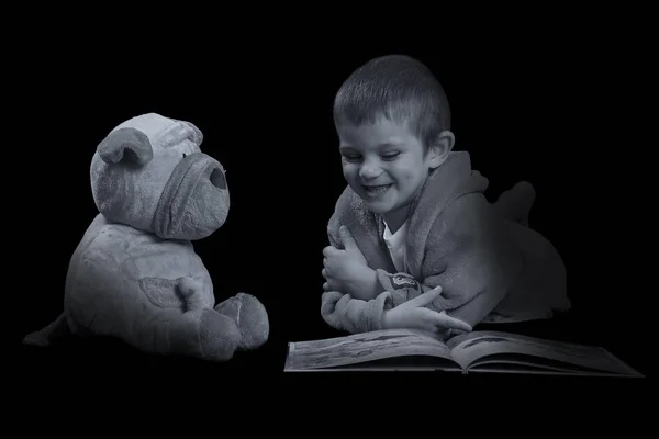 Garoto engraçado com um cachorro de pelúcia lendo um livro para a hora de dormir em arti — Fotografia de Stock