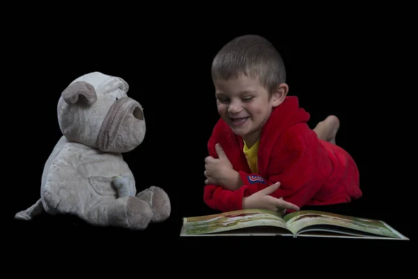 Funny boy with a stuffed dog reading a book for bed time — Stock Photo, Image