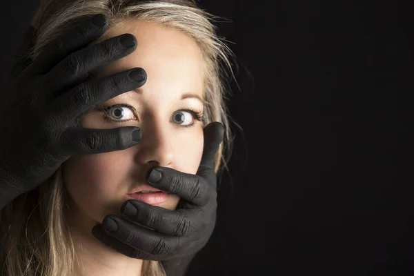 Mulher loira assustada agarrada por mãos negras no rosto — Fotografia de Stock