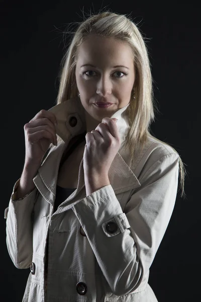 Beautiful blond woman in beige jacket in dark with selective lig Royalty Free Stock Photos