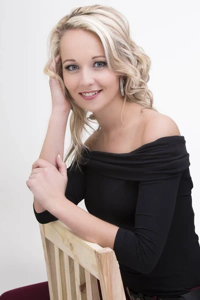 Beautiful blond woman in curly hair and black top sitting on woo Royalty Free Stock Images