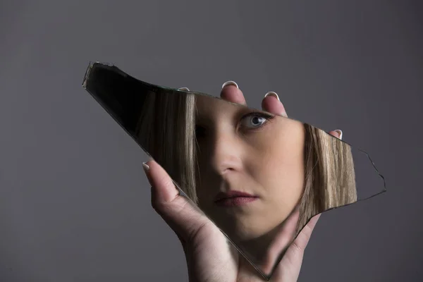 Mujer mirando su cara en fragmento de espejo roto —  Fotos de Stock