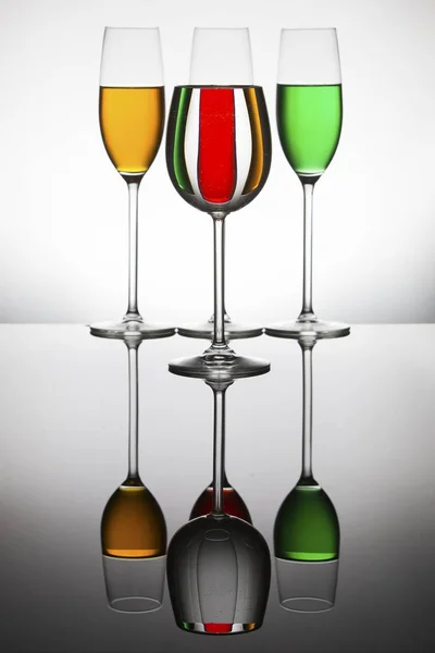 Wineglasses on a shiny surface with different colour fluids that — Stock Photo, Image