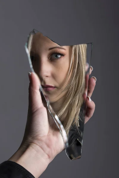 Mujer mirando su cara en fragmento de espejo roto —  Fotos de Stock