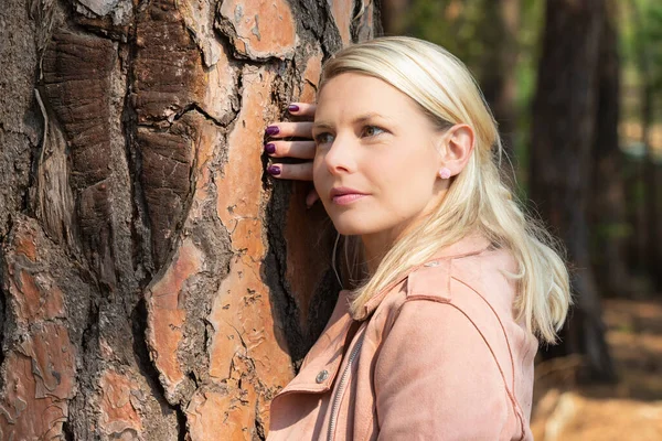 Portrait of a blonde woman next a tree with textured bark — Stock Photo, Image