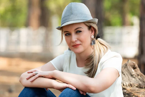 Portrait of a blonde woman with a white shirt and hat sitting ag — Stock Photo, Image