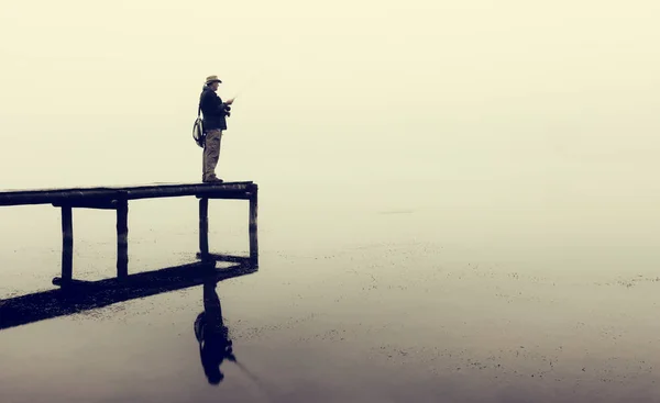 Man with fly-fishing gear catching a trout from jetty on a foggy — Stock Photo, Image