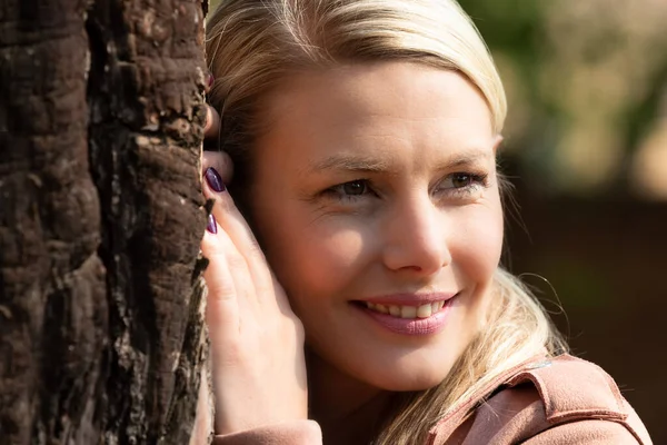 Portrait of a blonde woman next a tree with textured bark — Stock Photo, Image