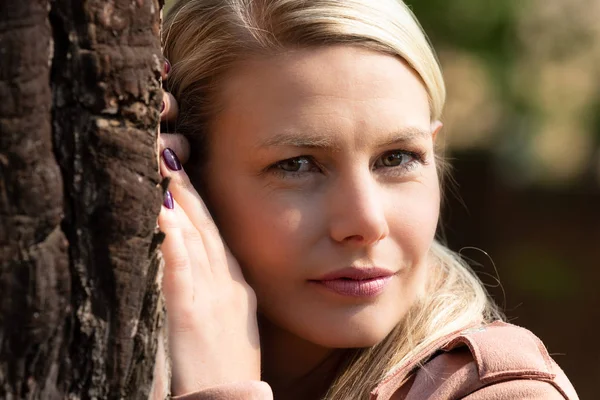 Portrait of a blonde woman next a tree with textured bark — Stock Photo, Image