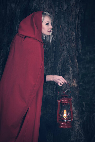 Attractive woman dressed a little red riding-hood walk in a dark forest with a lantern