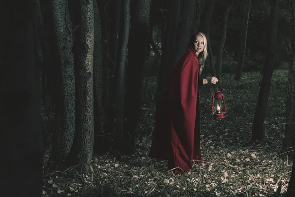 魅力的な女性は少し赤い乗馬を着て 提灯と暗い森の中を歩くフード — ストック写真