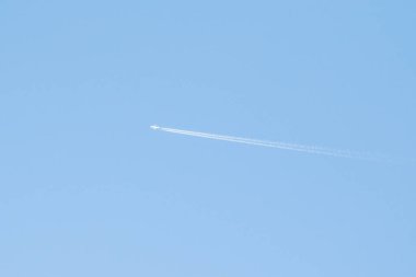 Mavi gökyüzündeki bir uçağın beyaz izi. Açık mavi gökyüzünde kanatlı bir yolcu uçağının izi.