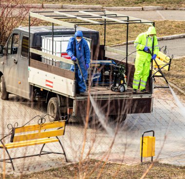 Petropavlovsk, Kazakistan - 4 Nisan 2020: sokak dezenfekte salgını. İşçi dolu bir araba parka kimyasal bir solüsyon sıkıyor..