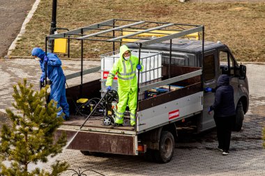 Petropavlovsk, Kazakistan - 4 Nisan 2020: sokak dezenfekte salgını. İşçi dolu bir araba parka kimyasal bir solüsyon sıkıyor..
