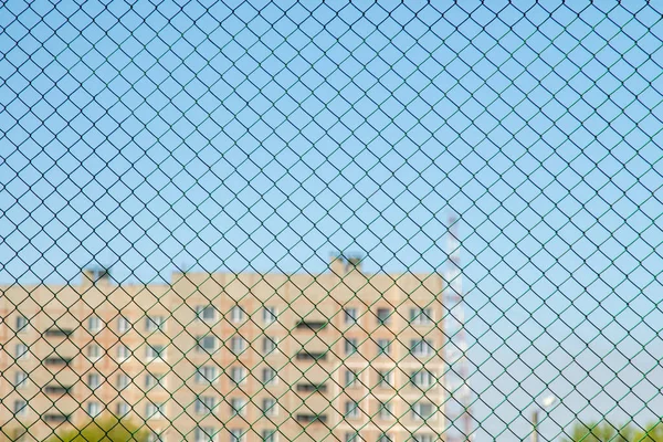 The metal mesh of the fence protecting the territory of the new microdistrict is in the background out of focus is a multi-story residential building. Ban on leaving the house, 2020, pandemic quarantine.