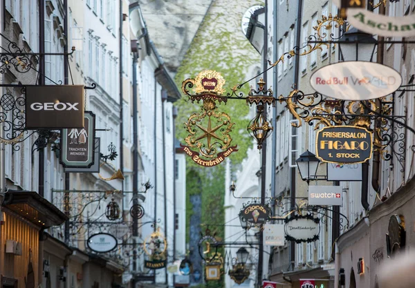 Winkelstraat in Salzburg - Getreidegasse met meerdere reclameborden. Capucijnenberg & Capucijnenklooster, is een van de oudste straten in Salzburg — Stockfoto