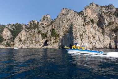 Gemilerde teknedeki turist ve Uçurumun kıyısında ve Capri Adası ile görüntüleyin. İtalya
