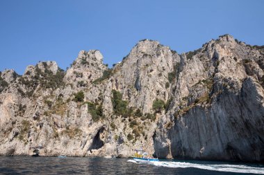 Gemilerde teknedeki turist ve Uçurumun kıyısında ve Capri Adası ile görüntüleyin. İtalya
