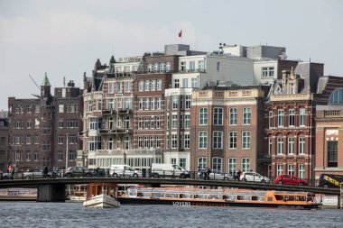 Amsterdam, Hollanda - 20 Nisan 2017: Cruise turist teknede Amsterdam, Hollanda, kanalda bir yaz gününde. İçinde belgili tanımlık geçmiş geleneksel evleri 