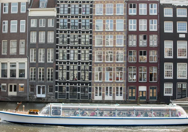 AMSTERDAM, NETHERLANDS - APRIL 20, 2017: Cruise tourist boat on a Damrak canal in Amsterdam, Netherlands, on a summer day. Traditional houses in the background