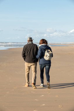  A woman and a man are walking on a sunny day along the beach in Katwijk. Netherlands clipart